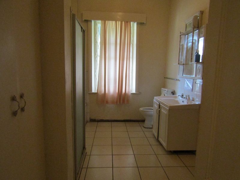 A functional bathroom featuring a vanity cabinet, toilet, and shower enclosure, with tiled flooring and a window fitted with a security gate.
