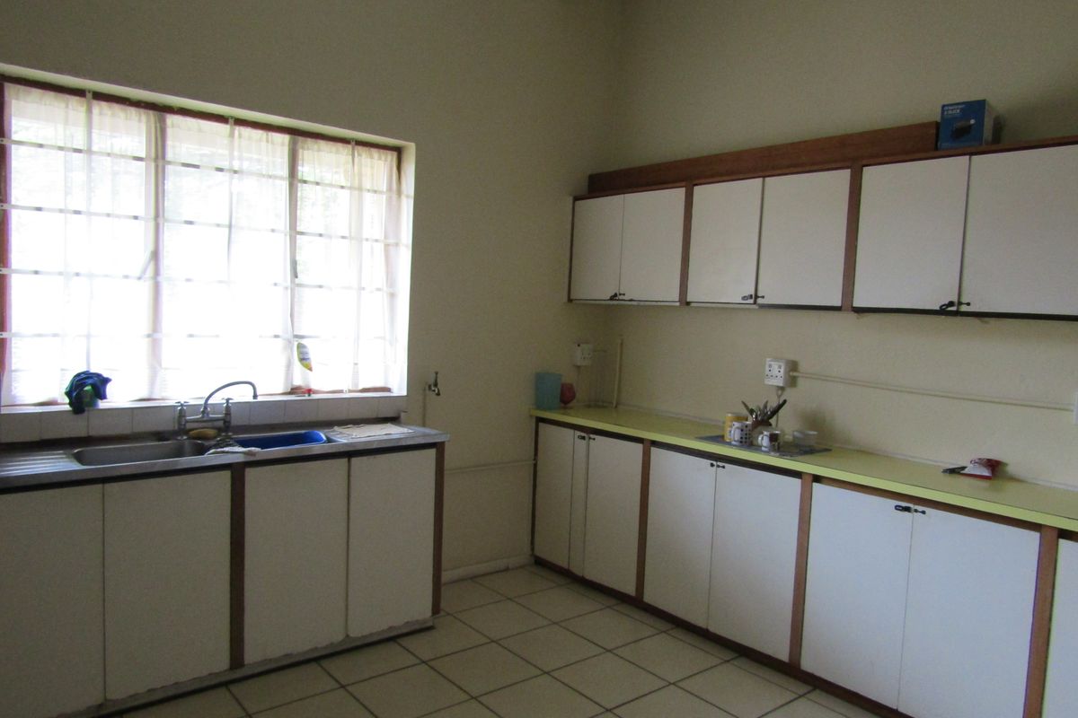 A functional kitchen space featuring extensive built-in cabinetry, laminate countertops, a stainless steel sink, and tiled flooring, offering potential for modern updates.