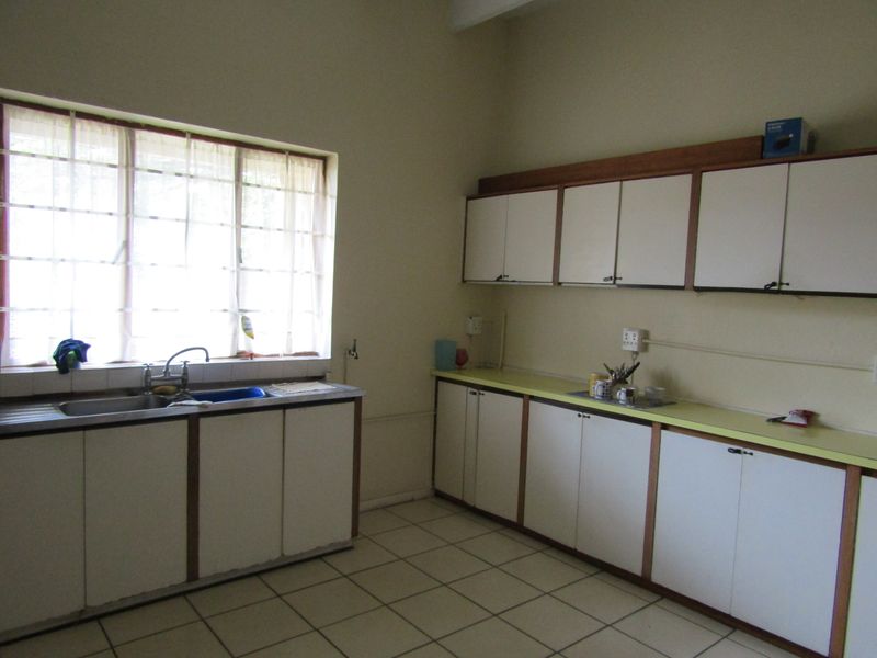 A functional kitchen space featuring extensive built-in cabinetry, laminate countertops, a stainless steel sink, and tiled flooring, offering potential for modern updates.