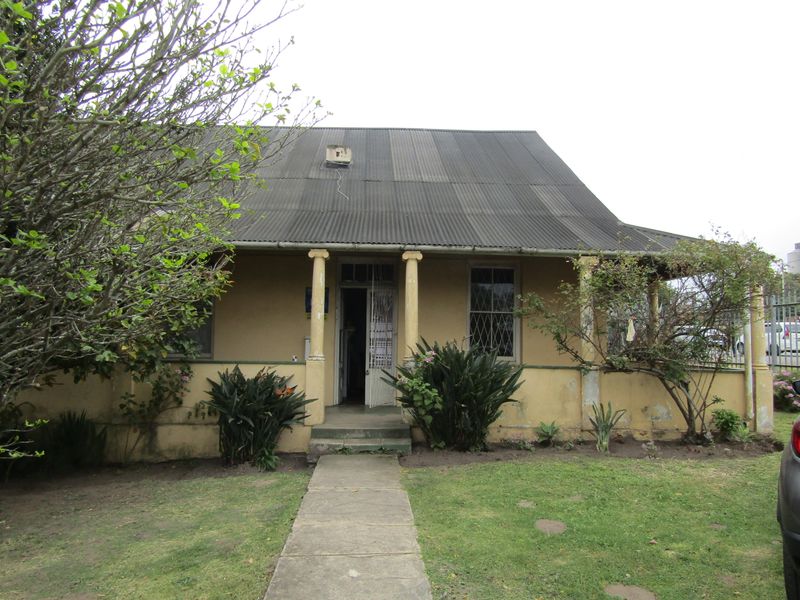 Front elevation of a commercial property featuring a covered veranda, classical columns, and a corrugated metal roof, showing signs of exterior wear.