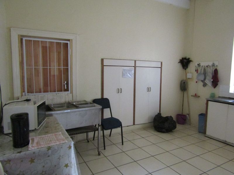 A functional scullery area featuring tiled flooring, built-in storage cupboards, and a stainless steel sink unit with a security gate on the window.