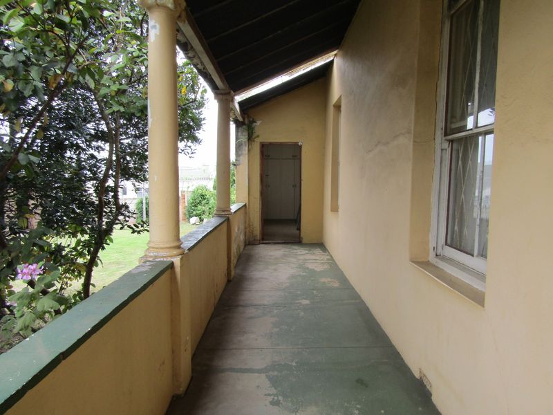 A covered outdoor veranda featuring concrete columns and a painted floor, showing signs of wear and requiring maintenance to the exterior finishes.