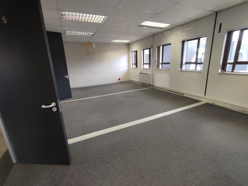 An empty office space featuring suspended ceilings, recessed lighting, carpeted flooring, and an integrated HVAC unit, requiring cosmetic updates.