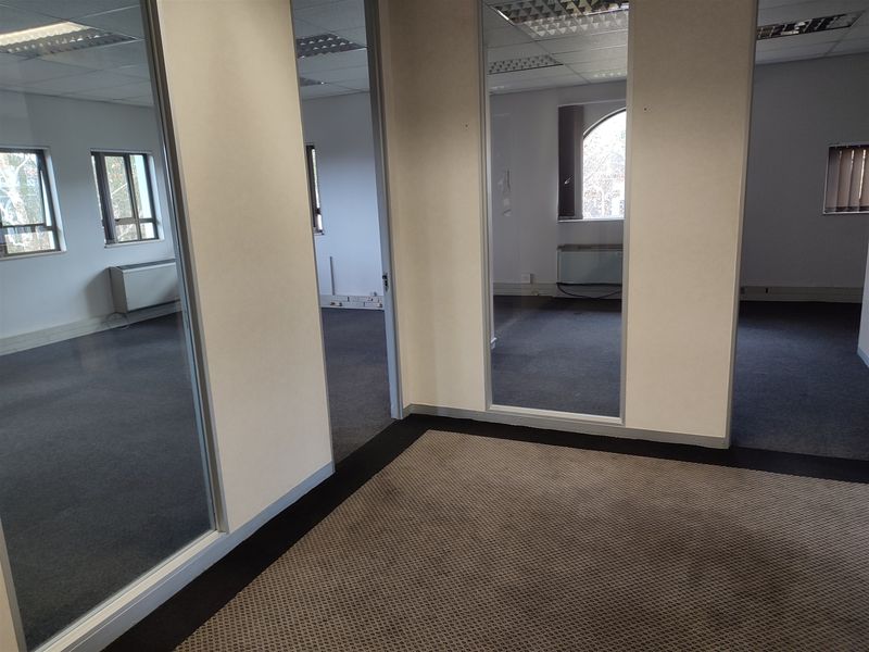 An empty office space featuring glass partitions, suspended ceilings, and carpeted flooring, offering a versatile layout for professional use.