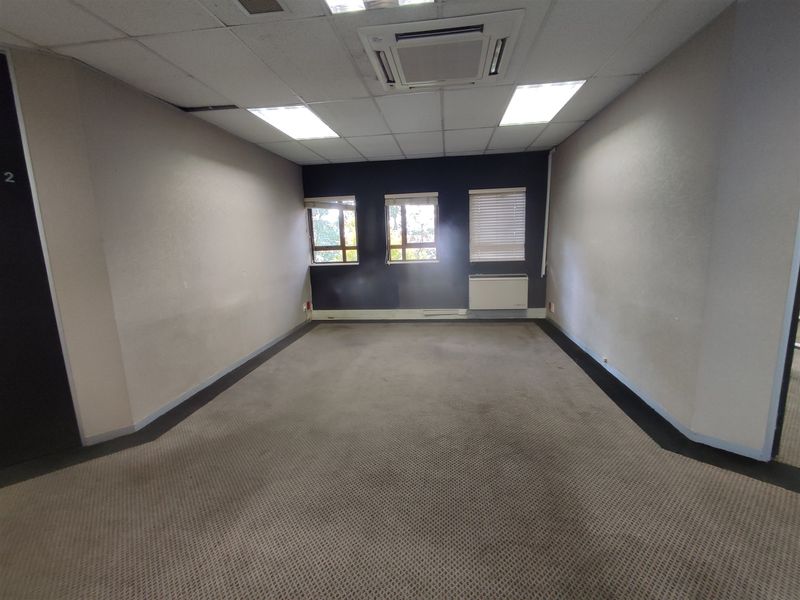 An empty office space featuring a suspended ceiling, recessed lighting, integrated air conditioning, and carpeted flooring with natural light from three windows.
