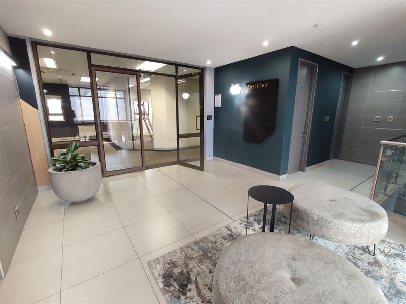 Modern office building lobby featuring tiled flooring, glass partition entrance, and professional signage leading to the first floor.