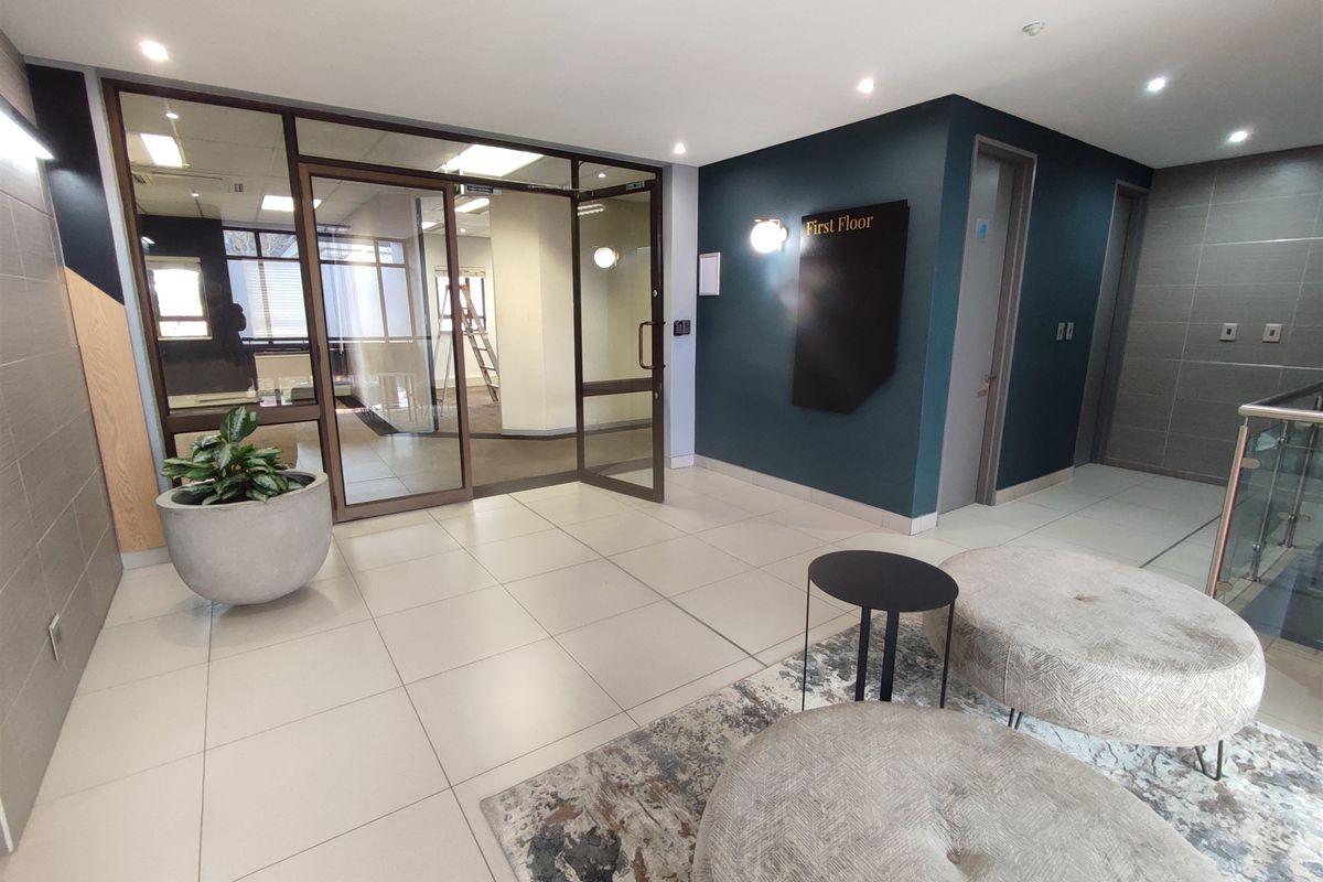 Modern office building lobby featuring tiled flooring, glass partition entrance, and professional signage leading to the first floor.