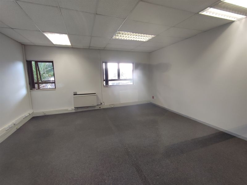 An empty, functional office space featuring a suspended ceiling, recessed lighting, carpeted flooring, and an integrated air conditioning unit.