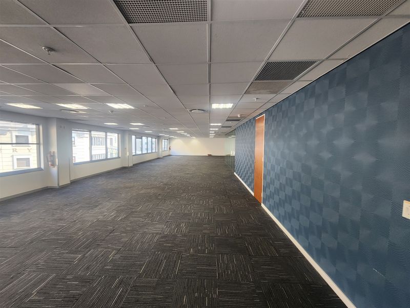 Spacious open-plan office area featuring carpeted flooring, suspended ceilings with recessed lighting, and a feature wall with textured wallpaper.