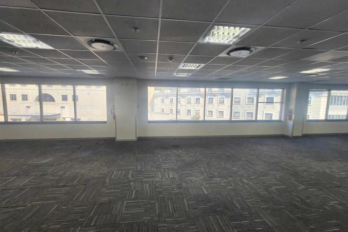 An empty, open-plan office space featuring suspended ceilings, recessed lighting, and large windows providing natural light and urban views.
