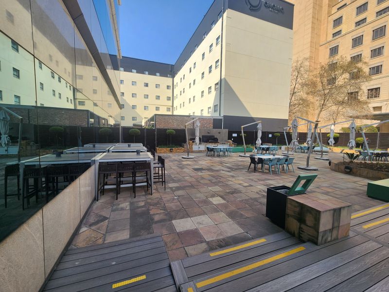 Spacious outdoor terrace featuring paved flooring, timber decking sections, and a glass-fronted building facade, suitable for office break-out or social gatherings.
