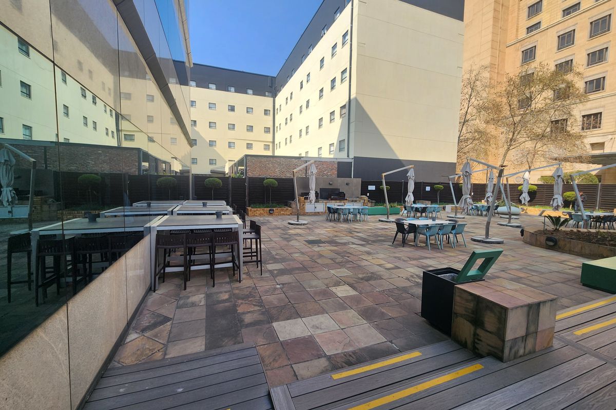 Spacious outdoor terrace featuring paved flooring, timber decking sections, and a glass-fronted building facade, suitable for office break-out or social gatherings.