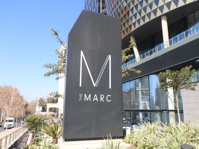 Exterior view of The Marc office complex featuring prominent building signage, modern glass facade, and landscaped grounds.