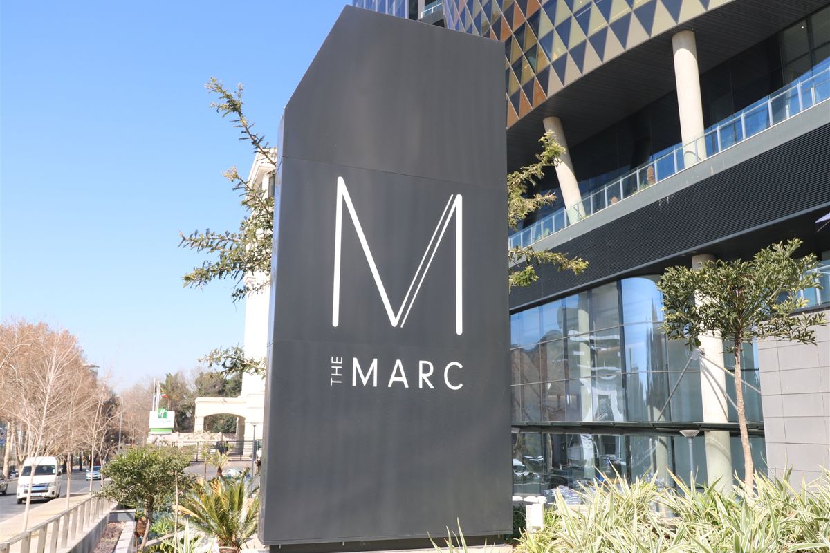 Exterior view of The Marc office complex featuring prominent building signage, modern glass facade, and landscaped grounds.