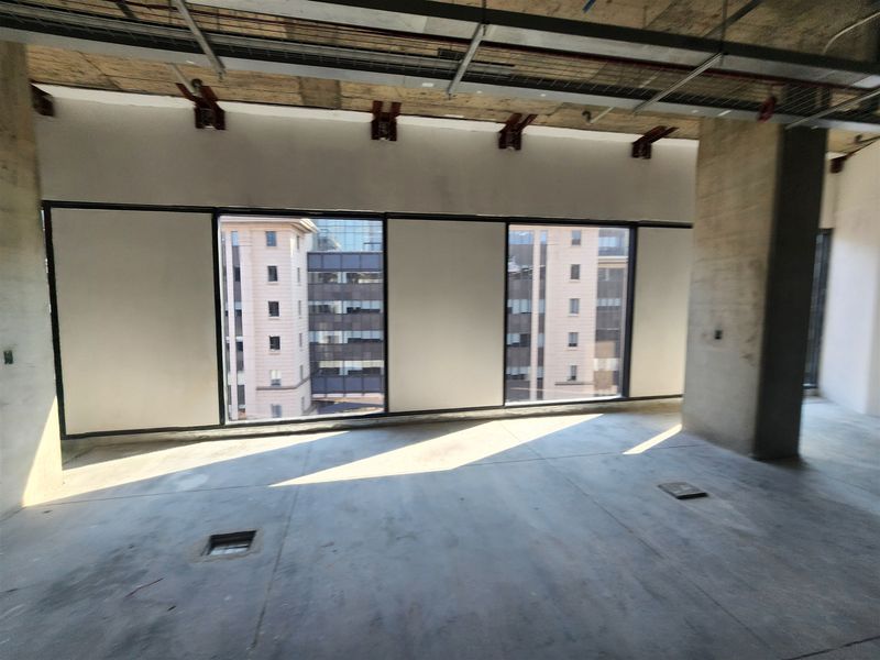 An unfinished open-plan office space featuring exposed concrete ceilings, large windows with urban views, and floor-level electrical access points.