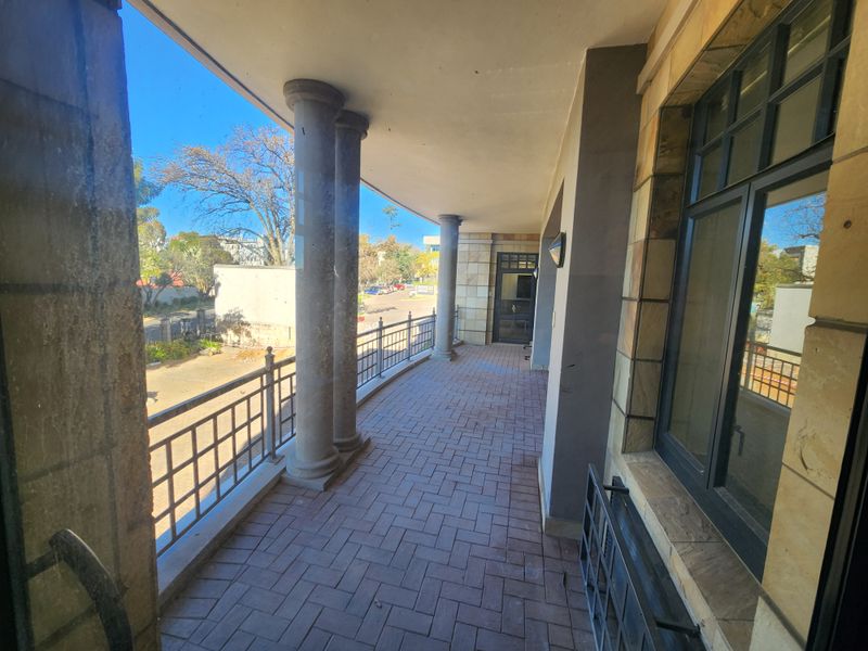 A covered outdoor balcony featuring stone columns, brick paving, and metal railings, providing an open-air transition space for the office building.