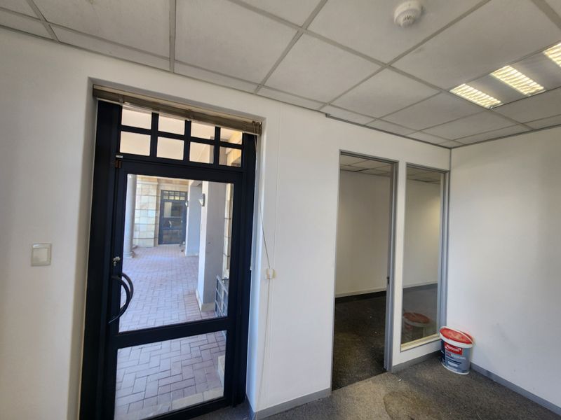 An empty office space featuring a suspended ceiling, recessed lighting, and a glass partition, providing a functional layout for professional use.