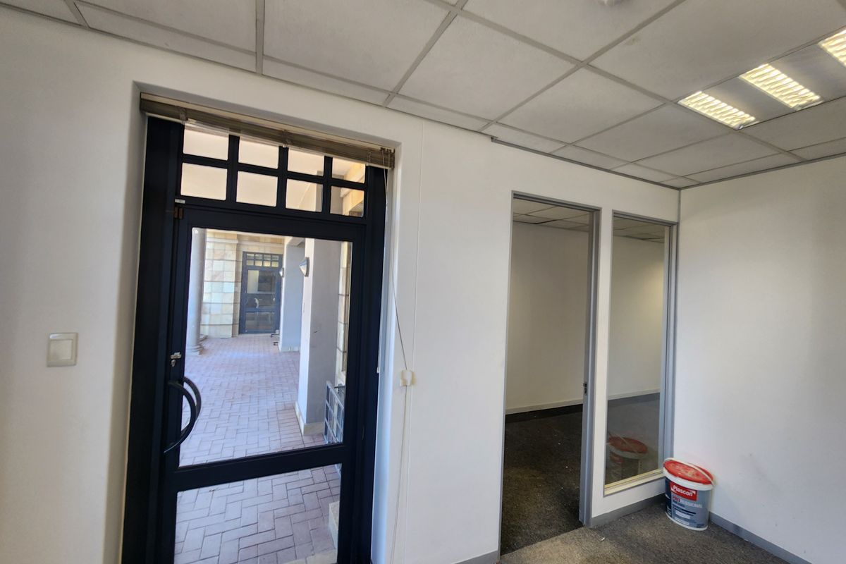An empty office space featuring a suspended ceiling, recessed lighting, and a glass partition, providing a functional layout for professional use.