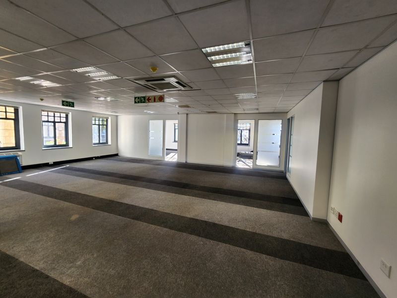 Spacious open-plan office area featuring a suspended ceiling, recessed lighting, ducted air conditioning, and large windows providing natural light.