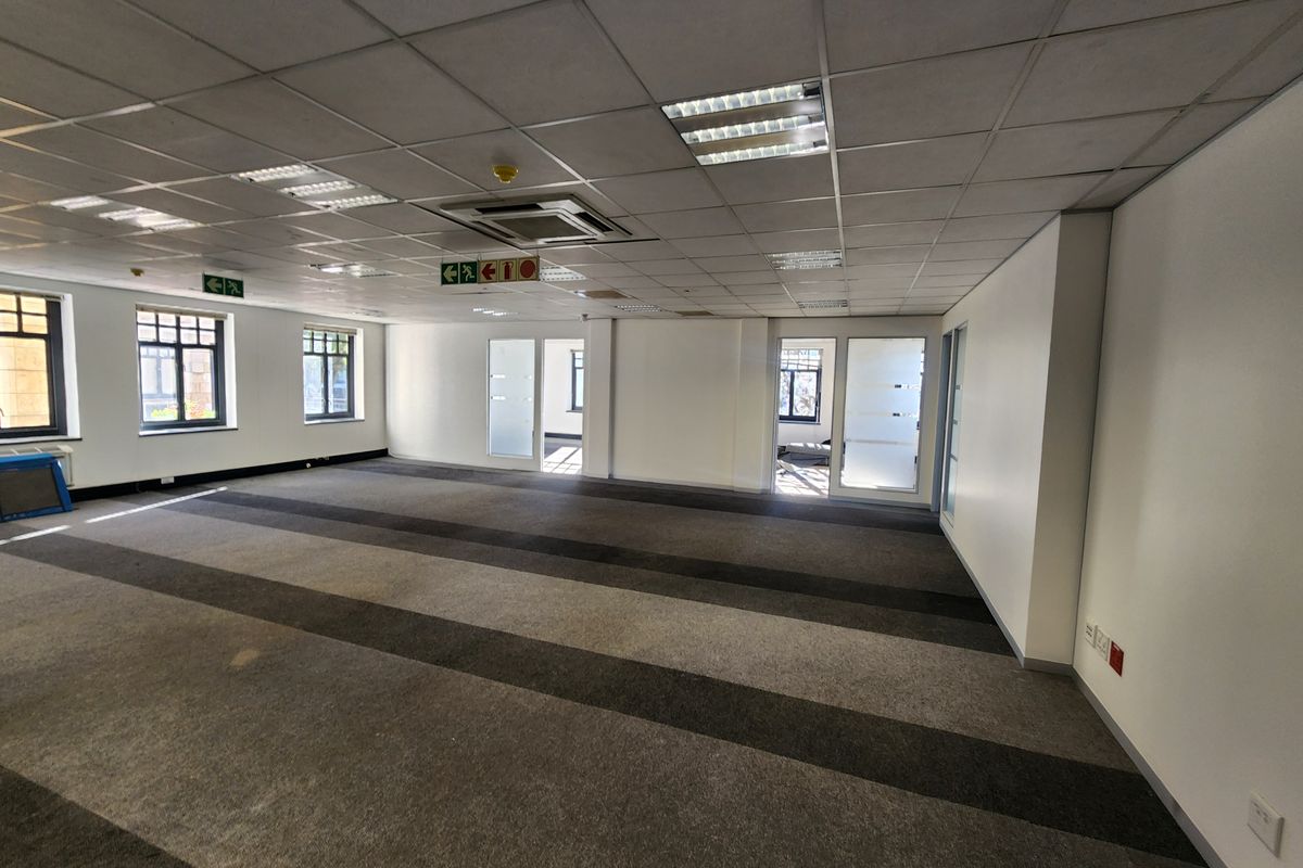Spacious open-plan office area featuring a suspended ceiling, recessed lighting, ducted air conditioning, and large windows providing natural light.