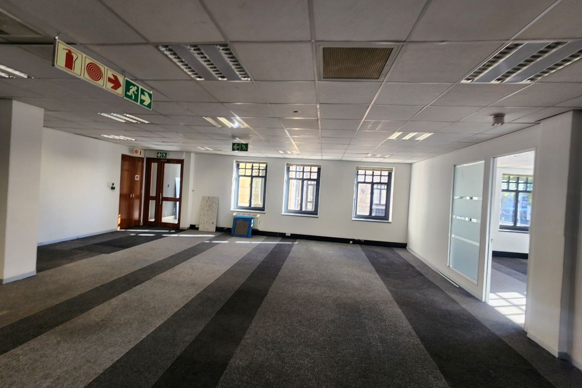 Spacious, open-plan office area featuring a suspended ceiling, recessed lighting, carpeted flooring, and glass partition doors, providing a versatile workspace.
