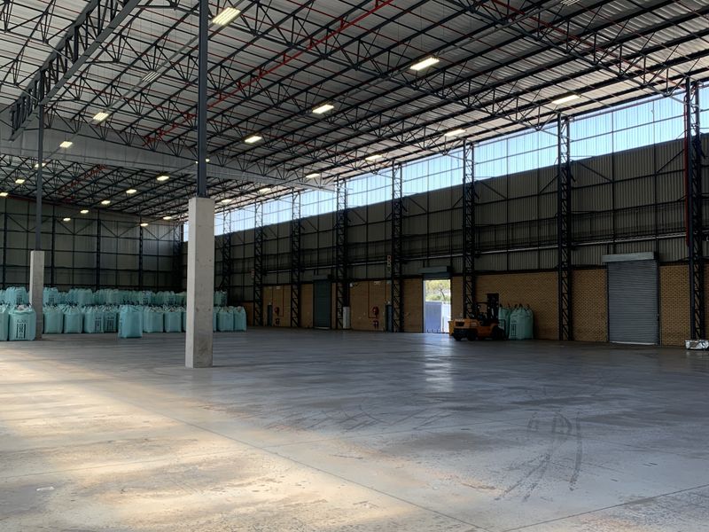 Spacious industrial warehouse featuring high ceilings with exposed steel trusses, polished concrete flooring, and large roller shutter access.