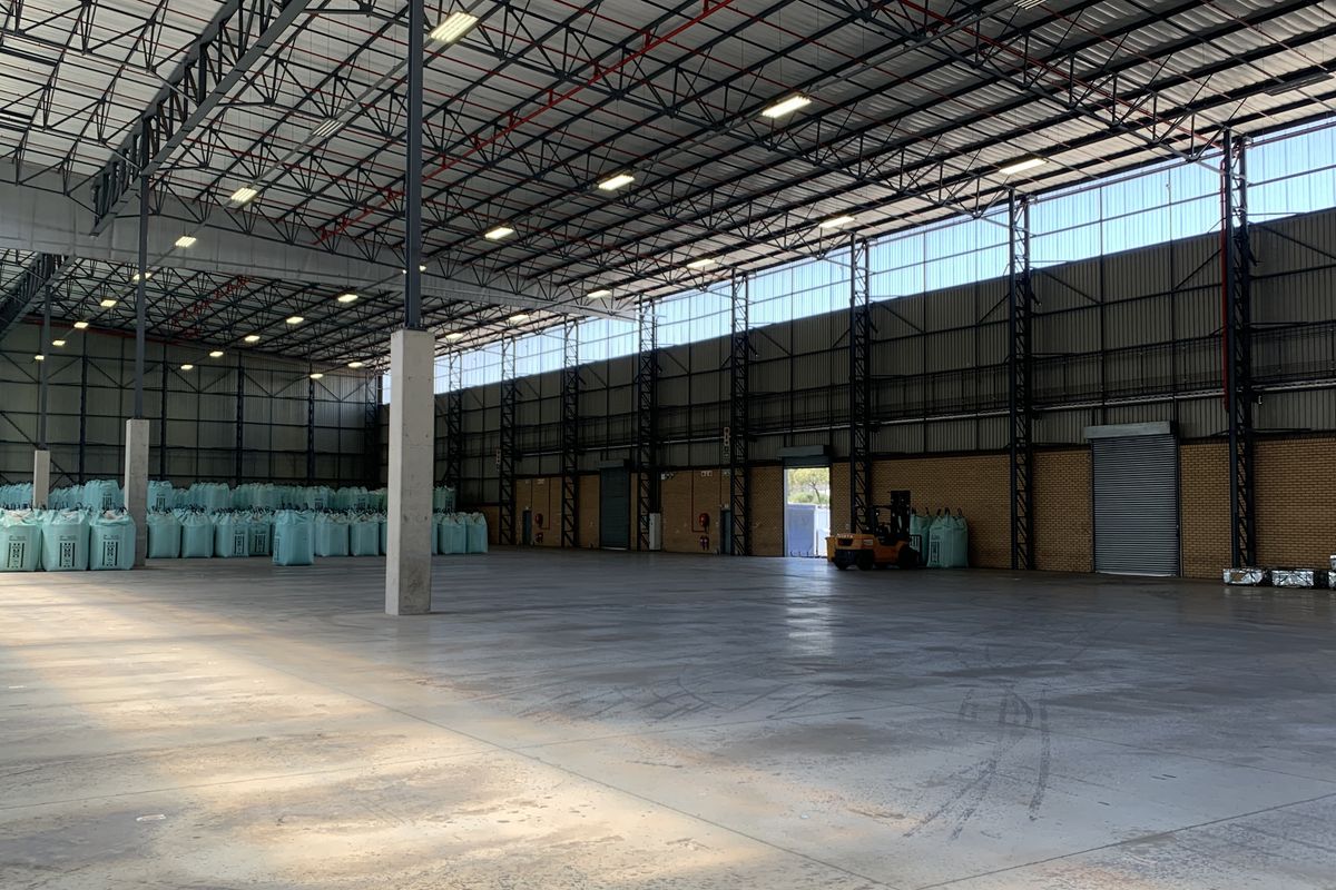 Spacious industrial warehouse featuring high ceilings with exposed steel trusses, polished concrete flooring, and large roller shutter access.