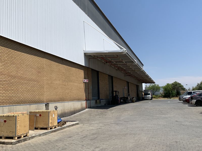 Industrial warehouse exterior featuring a brick and metal facade, loading canopy, roller shutter doors, and a spacious paved yard area.