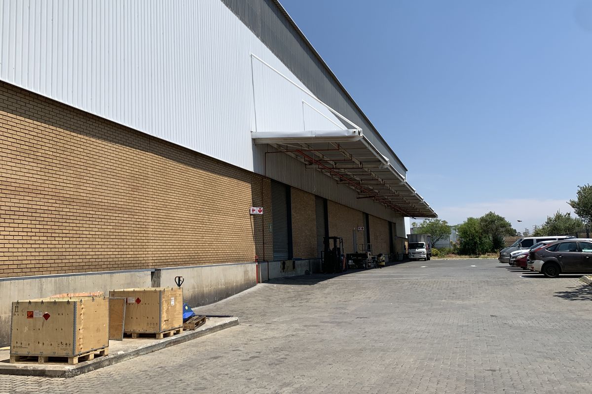Industrial warehouse exterior featuring a brick and metal facade, loading canopy, roller shutter doors, and a spacious paved yard area.