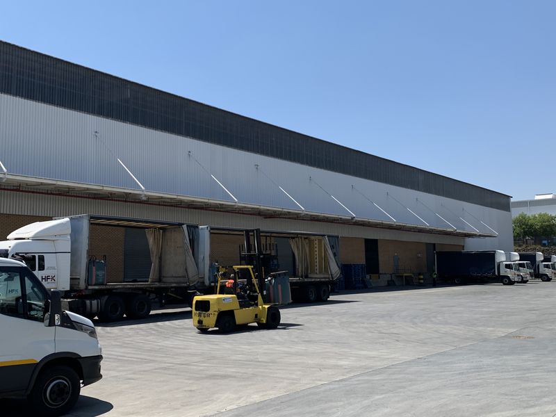 Industrial warehouse exterior featuring a large concrete loading yard, multiple roller shutter doors, and a protective canopy for efficient logistics operations.