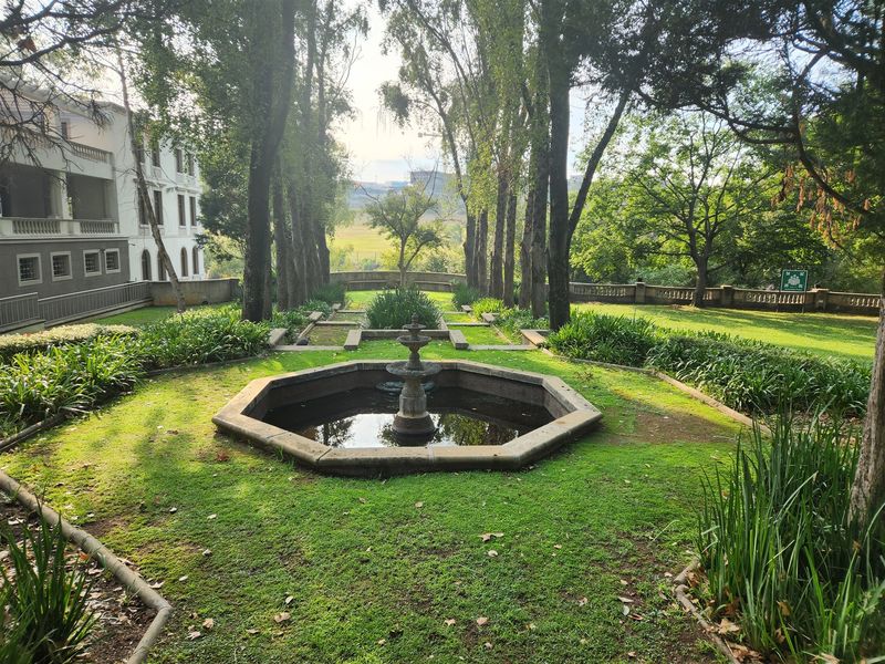 A well-maintained landscaped garden featuring a central stone fountain, mature trees, and stone balustrade detailing, providing a serene outdoor space.