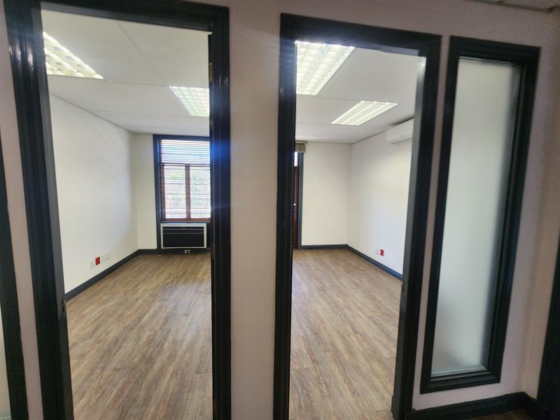 Two vacant office spaces featuring wood-look flooring, suspended ceilings with recessed lighting, and integrated air conditioning units, offering a clean and professional work environment.