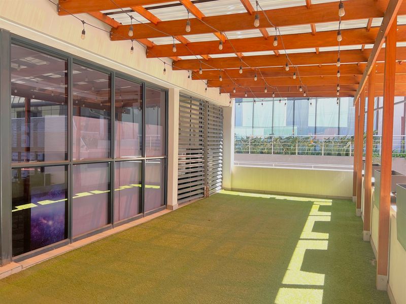 A well-maintained covered balcony featuring a timber pergola, integrated string lighting, artificial turf flooring, and modern aluminium-framed glass doors.