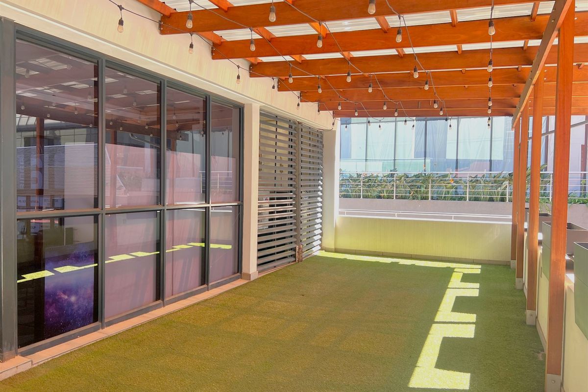 A well-maintained covered balcony featuring a timber pergola, integrated string lighting, artificial turf flooring, and modern aluminium-framed glass doors.