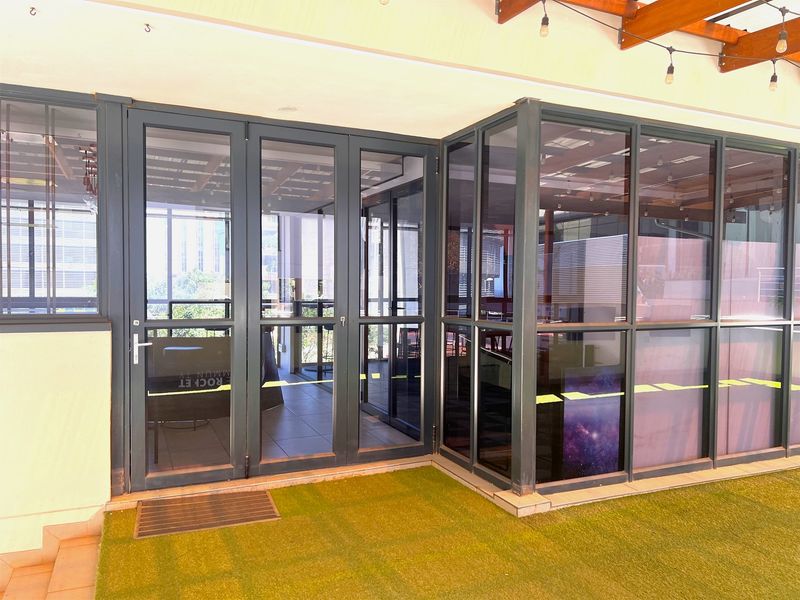 A modern covered patio area featuring aluminium-framed glass doors, a timber pergola with string lighting, and artificial turf flooring.