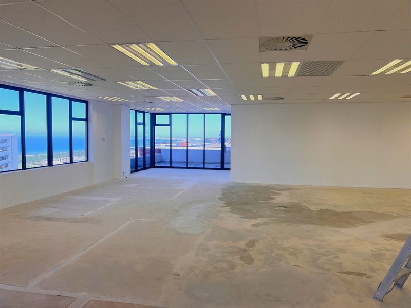 Spacious open-plan office area featuring large windows with ocean views, suspended ceilings, and unfinished concrete flooring ready for custom finishes.