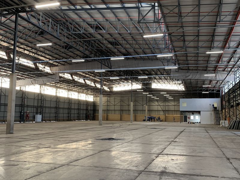 Expansive industrial warehouse space featuring high ceilings with exposed steel trusses, polished concrete flooring, integrated fire suppression, and a mezzanine office area.