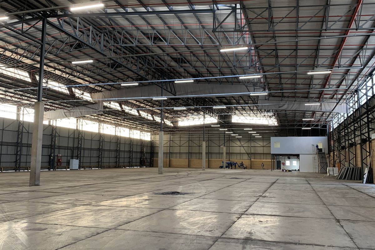 Expansive industrial warehouse space featuring high ceilings with exposed steel trusses, polished concrete flooring, integrated fire suppression, and a mezzanine office area.