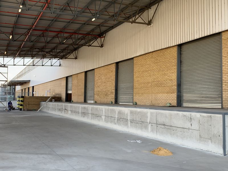 Industrial loading bay area featuring a concrete dock, multiple roller shutter doors, and an expansive covered steel roof structure.