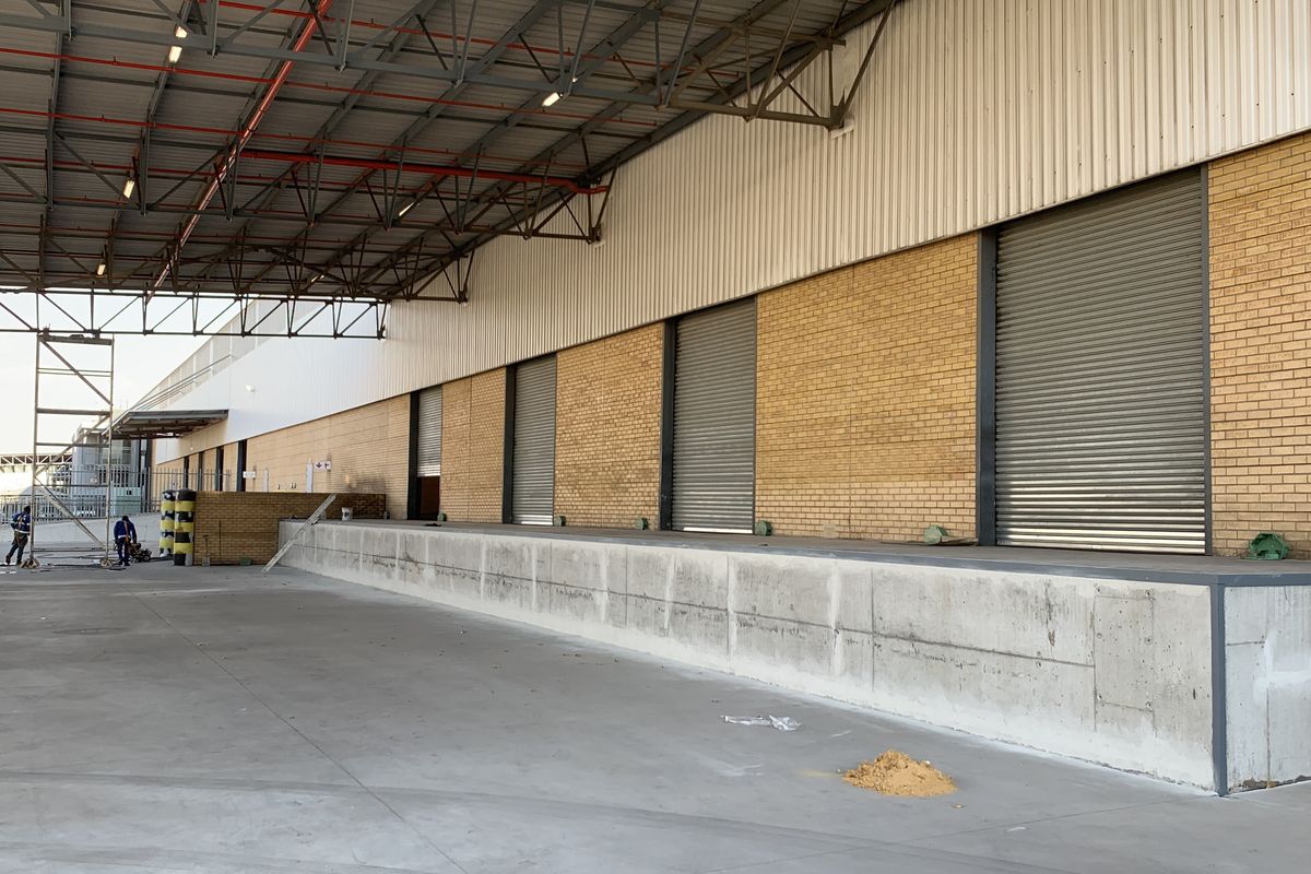 Industrial loading bay area featuring a concrete dock, multiple roller shutter doors, and an expansive covered steel roof structure.