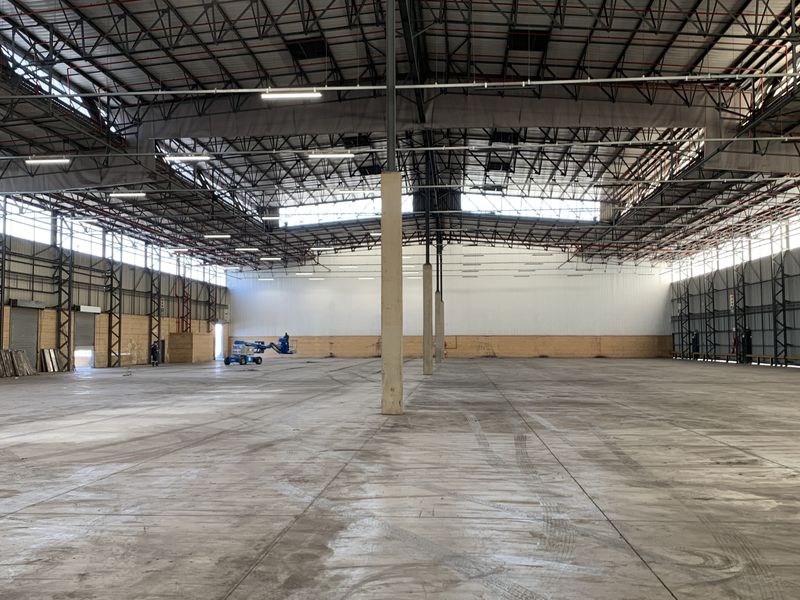 Large industrial warehouse space featuring high ceilings with exposed steel trusses, polished concrete flooring, and multiple roller shutter access points.