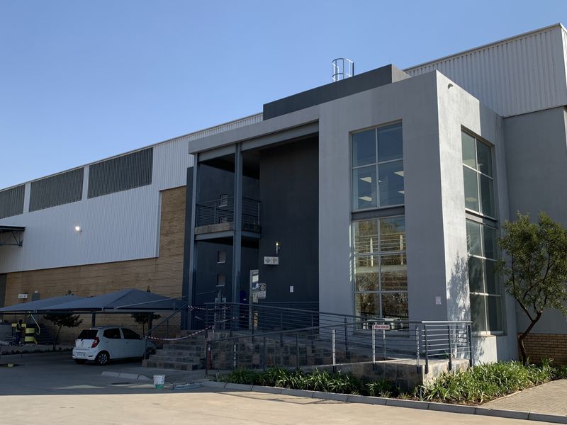 Modern industrial facility featuring a combination of brick and metal cladding, large glass windows, a concrete access ramp, and integrated covered parking.