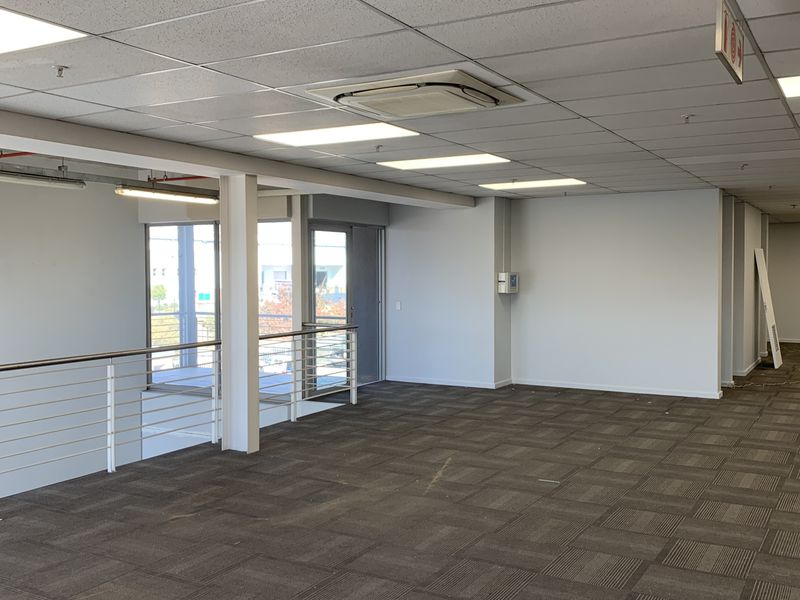 Spacious open-plan office area featuring suspended ceilings, recessed lighting, integrated air conditioning, and carpet tile flooring with a mezzanine-style balustrade.
