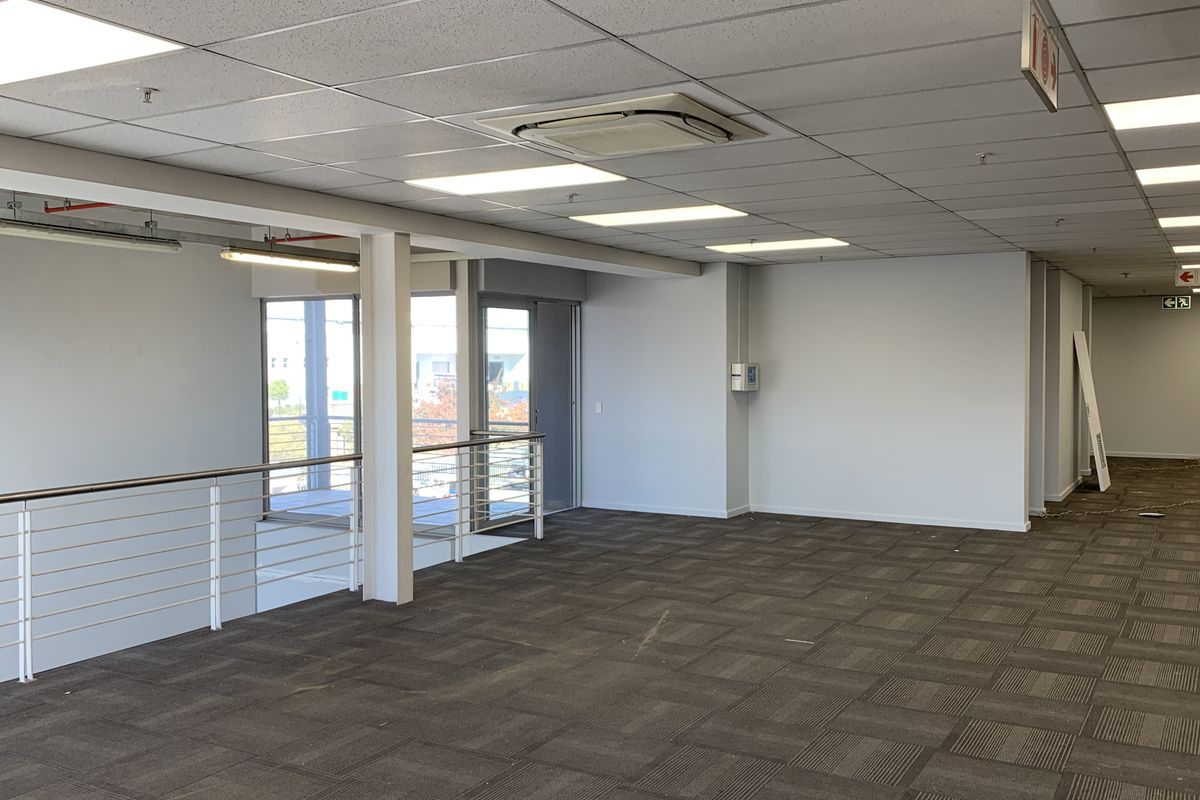Spacious open-plan office area featuring suspended ceilings, recessed lighting, integrated air conditioning, and carpet tile flooring with a mezzanine-style balustrade.
