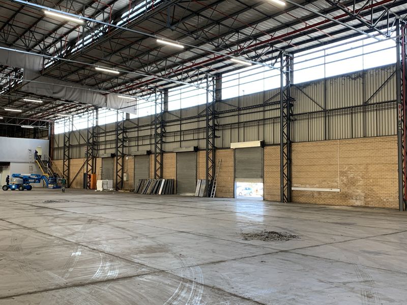 Spacious industrial warehouse featuring high ceilings, steel truss construction, multiple roller shutter doors, and a mezzanine level, suitable for logistics or manufacturing operations.