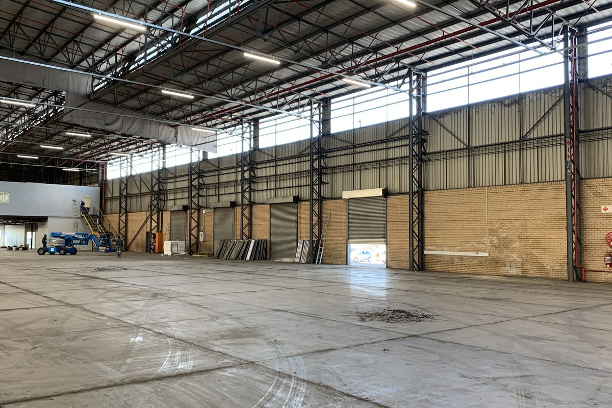Spacious industrial warehouse featuring high ceilings, steel truss construction, multiple roller shutter doors, and a mezzanine level, suitable for logistics or manufacturing operations.