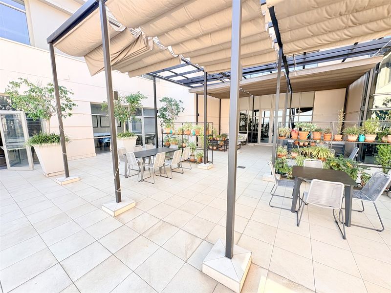 A spacious outdoor patio area featuring a retractable pergola, tiled flooring, and direct access to the office building through large glass doors.