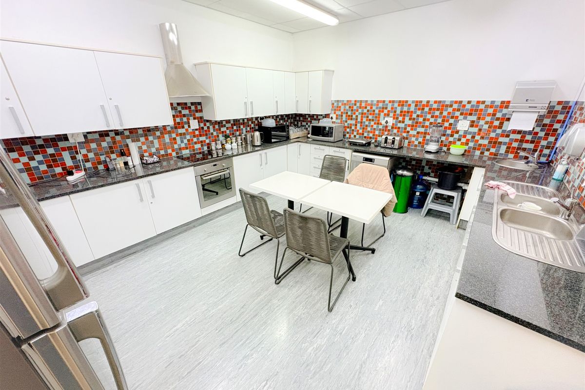 A functional office kitchen featuring white cabinetry, granite countertops, a mosaic tile backsplash, and integrated appliances, providing a practical break area for staff.