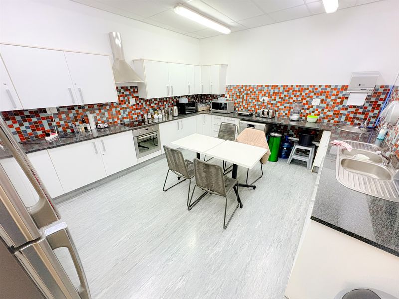 A functional office kitchen featuring white cabinetry, granite countertops, a mosaic tile backsplash, and integrated appliances, providing a practical break area for staff.