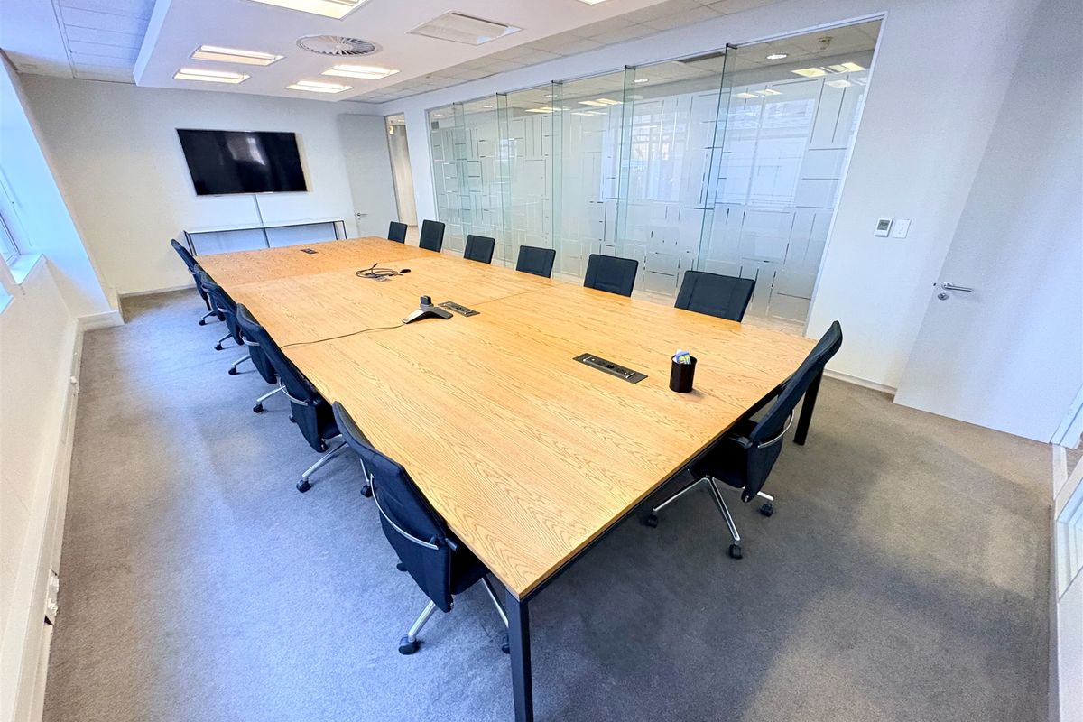 A professional boardroom featuring a large wooden conference table, glass partition walls, and recessed ceiling lighting, suitable for corporate meetings.